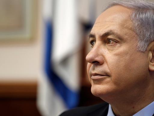 Portrait von Benjamin Netanjahu, im Hintergrund in der Unschärfe die israelische Flagge