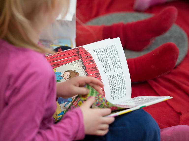 Ein Mädchen liest in einer Kita in einem Kinderbuch.