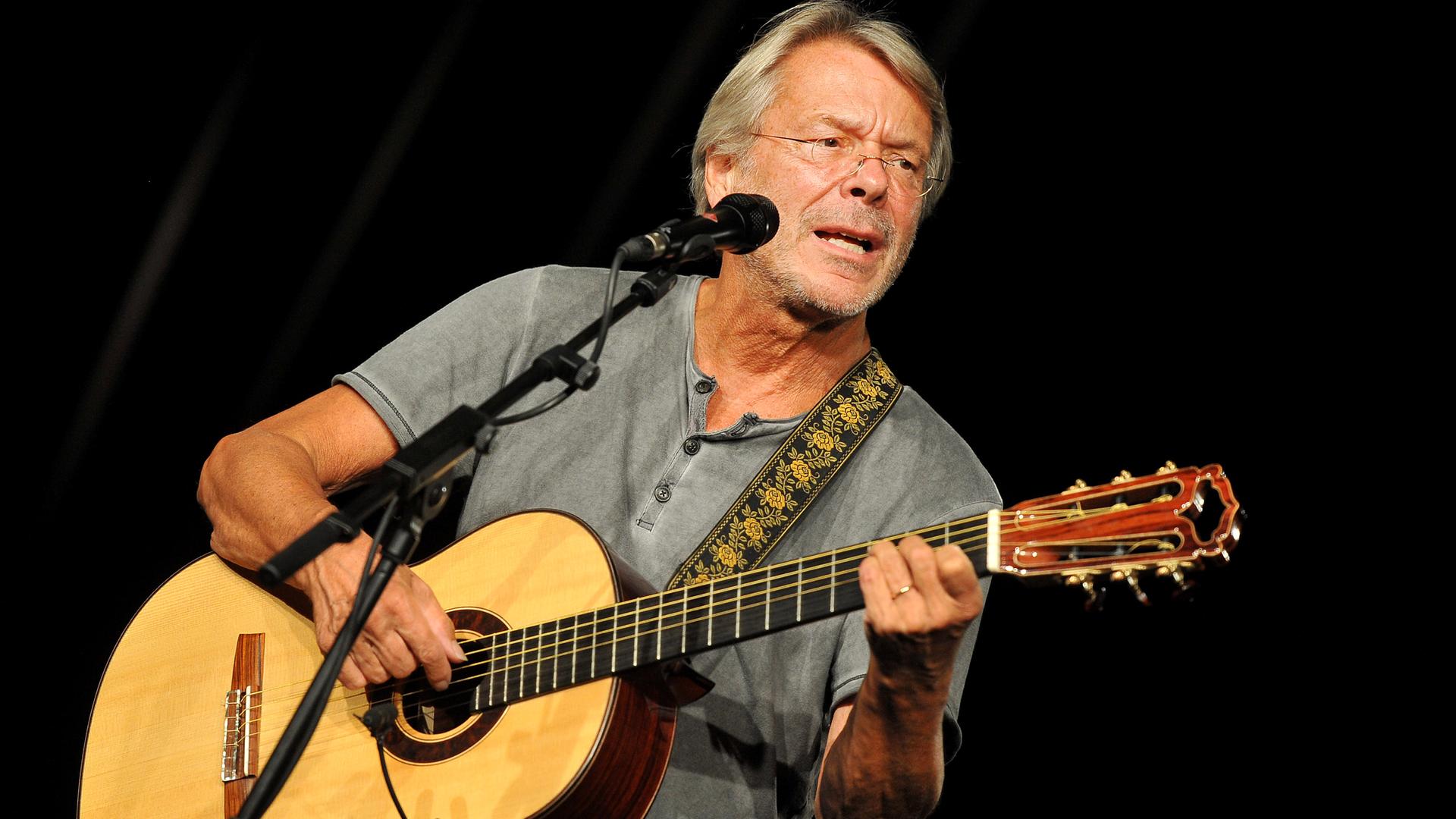 Reinhard Mey singt mit einer Gitarre in der Hand. Reinhard Mey singt mit einer Gitarre in der Hand.