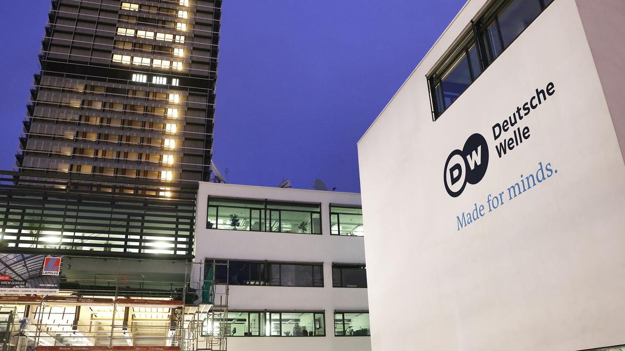 Der Sitz der Deutschen Welle in Bonn: Im Vordergrund rechts ist der Schriftzug des Senders auf einer Hauswand zu sehen, links im Bild steht ein erleuchtetes Hochhaus.