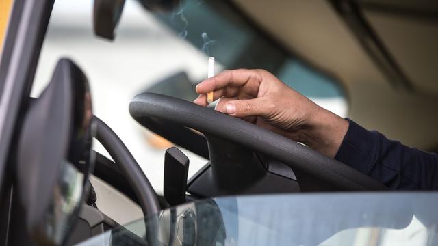 Ein Mann hat seine Hand auf dem Lenkrad eines Lkw abgelegt. Er hält eine Zigarette zwischen den Fingern.