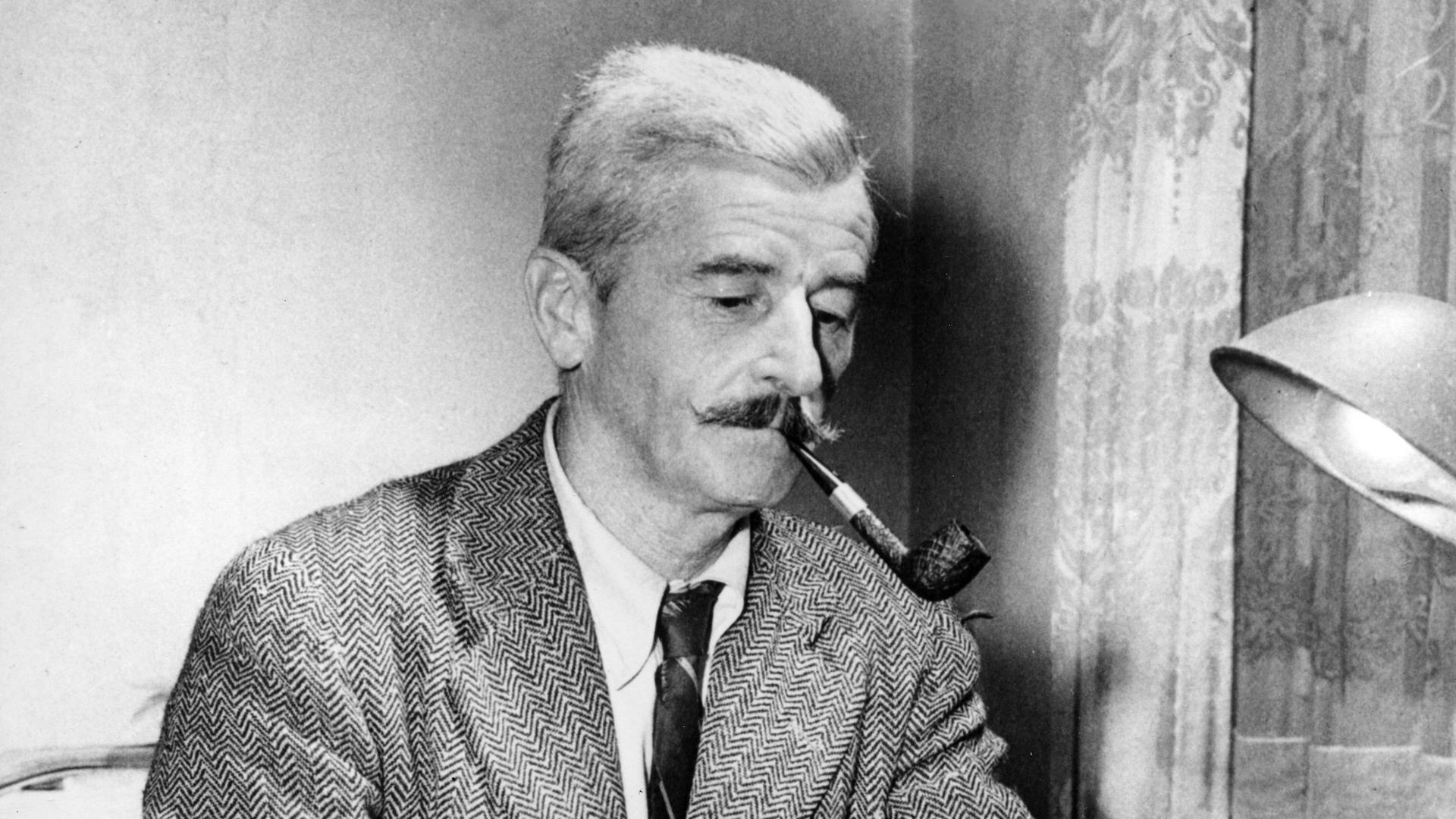 Das Schwarz-Weiß-Foto zeigt William Faulkner an seiner Schreibmaschine. Er trägt ein Tweed-Sakko und Schlips, raucht Pfeife und schaut konzentriert auf das eingespannte Blatt Papier.