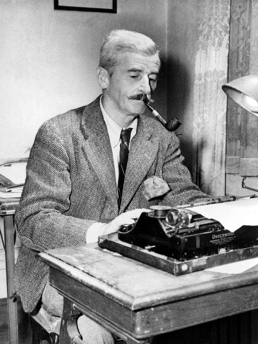 Das Schwarz-Weiß-Foto zeigt William Faulkner an seiner Schreibmaschine. Er trägt ein Tweed-Sakko und Schlips, raucht Pfeife und schaut konzentriert auf das eingespannte Blatt Papier.