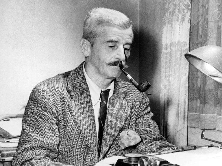 Das Schwarz-Weiß-Foto zeigt William Faulkner an seiner Schreibmaschine. Er trägt ein Tweed-Sakko und Schlips, raucht Pfeife und schaut konzentriert auf das eingespannte Blatt Papier.