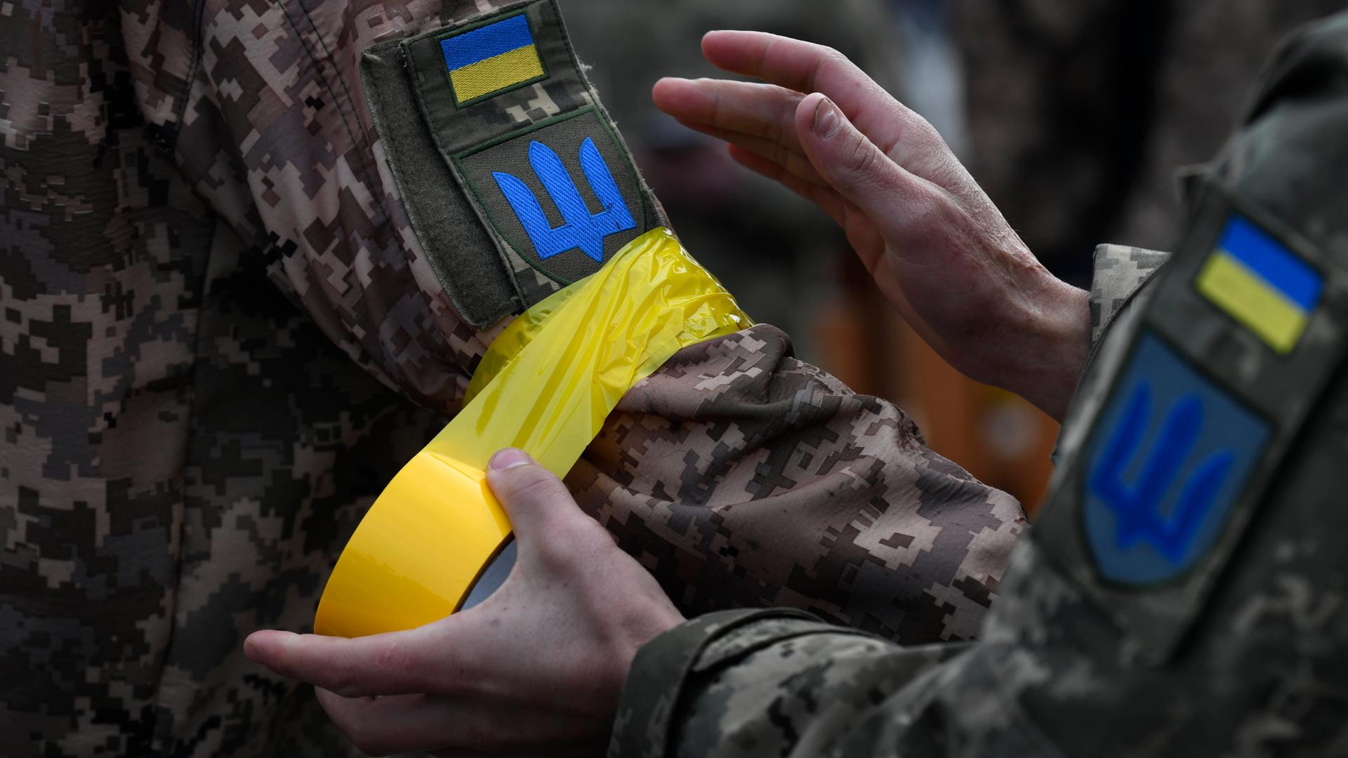 Ein ukrainischer Soldat macht einem Kameraden gelbes Klebeband an den Arm als Zeichen der Zugehörigkeit zu den regulären Streitkräften.