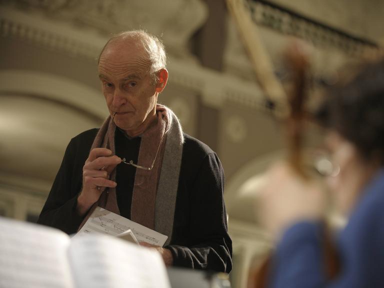 Christian Wolff steht nachdenklich mit Noten in der Hand vor einem Orchestermitglied