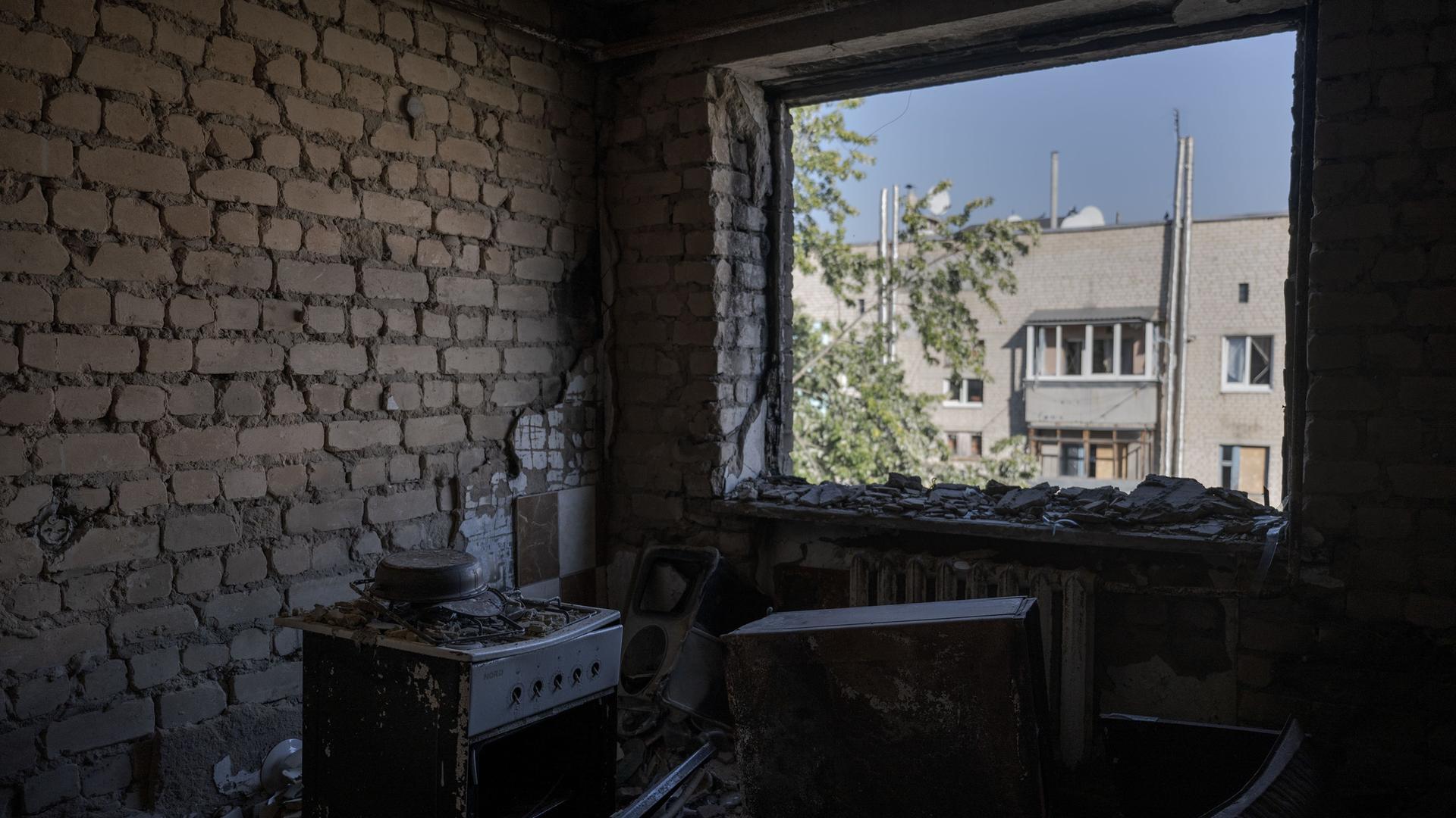 Das Bild zeigt ein zerstörtes Gebäude nach einem russischem Angriff von innen. Zu sehen sind die Reste einer Küche, dahinter ein zerstörtes Fenster.