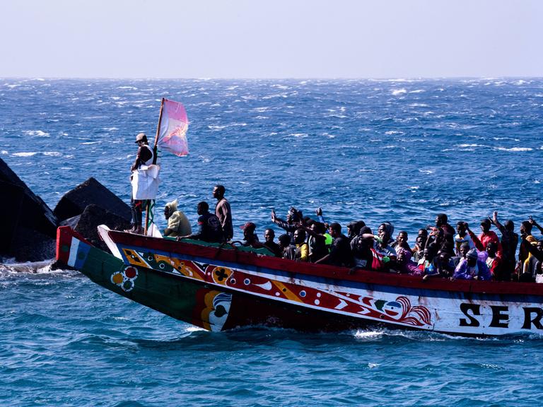 Eine Gruppe von Migranten feiert, dass sie die Überfahrt von Afrika nach Europa überlebt haben. Sie winken vom übervollen Boot. 358 Menschen erreichten im Laufe von drei Stunden die Kanareninsel El Hierro am 22. August 2024.