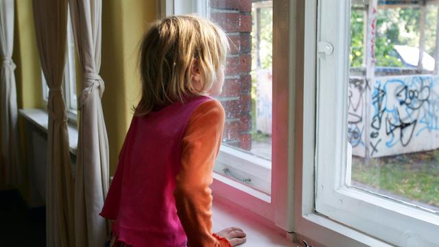 Ein kleines Mädchen schaut nachdenklich aus einem Fenster.