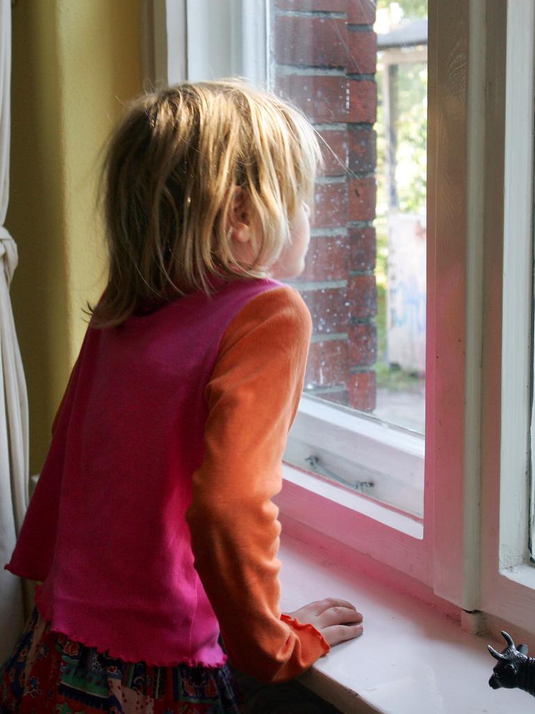Ein kleines Mädchen schaut nachdenklich aus einem Fenster.