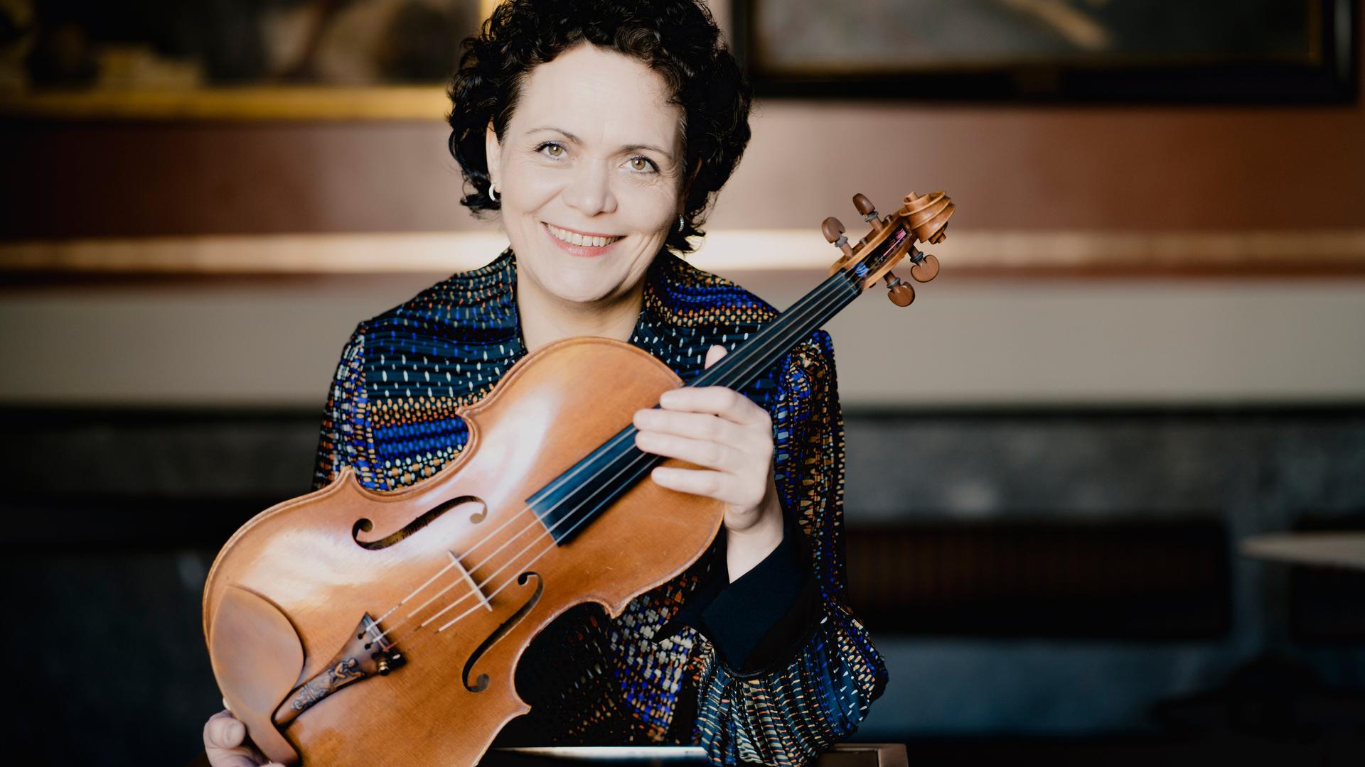 Eine Frau, die Bratschistin Tabea Zimmermann, hält eine Bratsche vor ihre Brust und lächelt