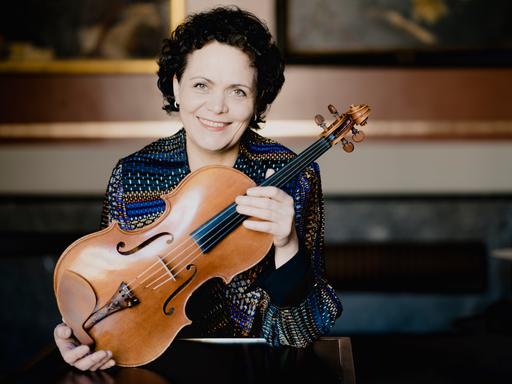 Eine Frau, die Bratschistin Tabea Zimmermann, hält eine Bratsche vor ihre Brust und lächelt