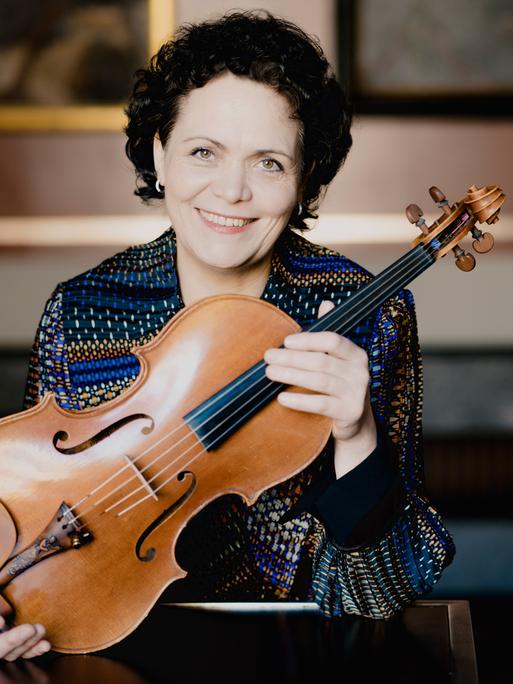 Eine Frau, die Bratschistin Tabea Zimmermann, hält eine Bratsche vor ihre Brust und lächelt