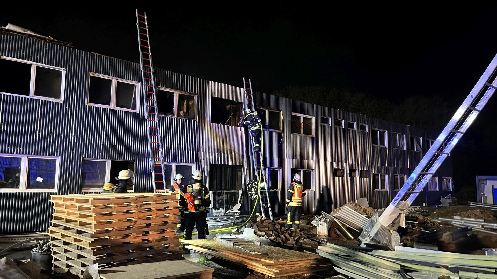 Feuerwehrleute löschen den Brand, Leitern stehen an der zweistöckigen Containeranlage. Feuerwehrleute löschen den Brand, Leitern stehen an der zweistöckigen Containeranlage.