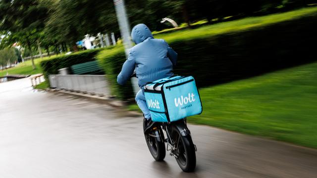 Ein Fahrradkurier von Wolt fährt im Anorak bei Herbstwetter eine Straße entlang. 