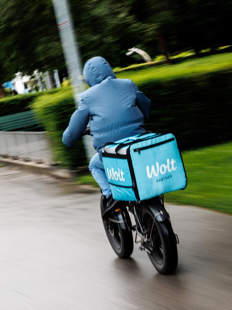 Ein Fahrradkurier von Wolt fährt im Anorak bei Herbstwetter eine Straße entlang. 