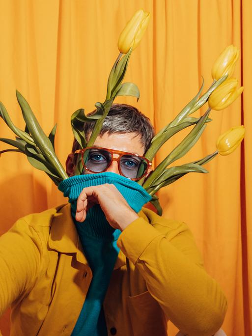 Ein Mann vor einem gelben Hintergrund mit gelben Tulpen in seinem Pullover