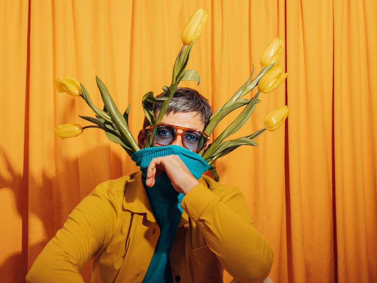 Ein Mann vor einem gelben Hintergrund mit gelben Tulpen in seinem Pullover