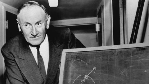 Der Schweizer Astrophysiker Fritz Zwicky, aufgenommen 1956 in Pasadena am California Insitute of Technology: hier erklärt er anhand  eines Schaubildes, wie der Planet Jupiter aus seiner Umlaufbahn katapuliert werden könnte.