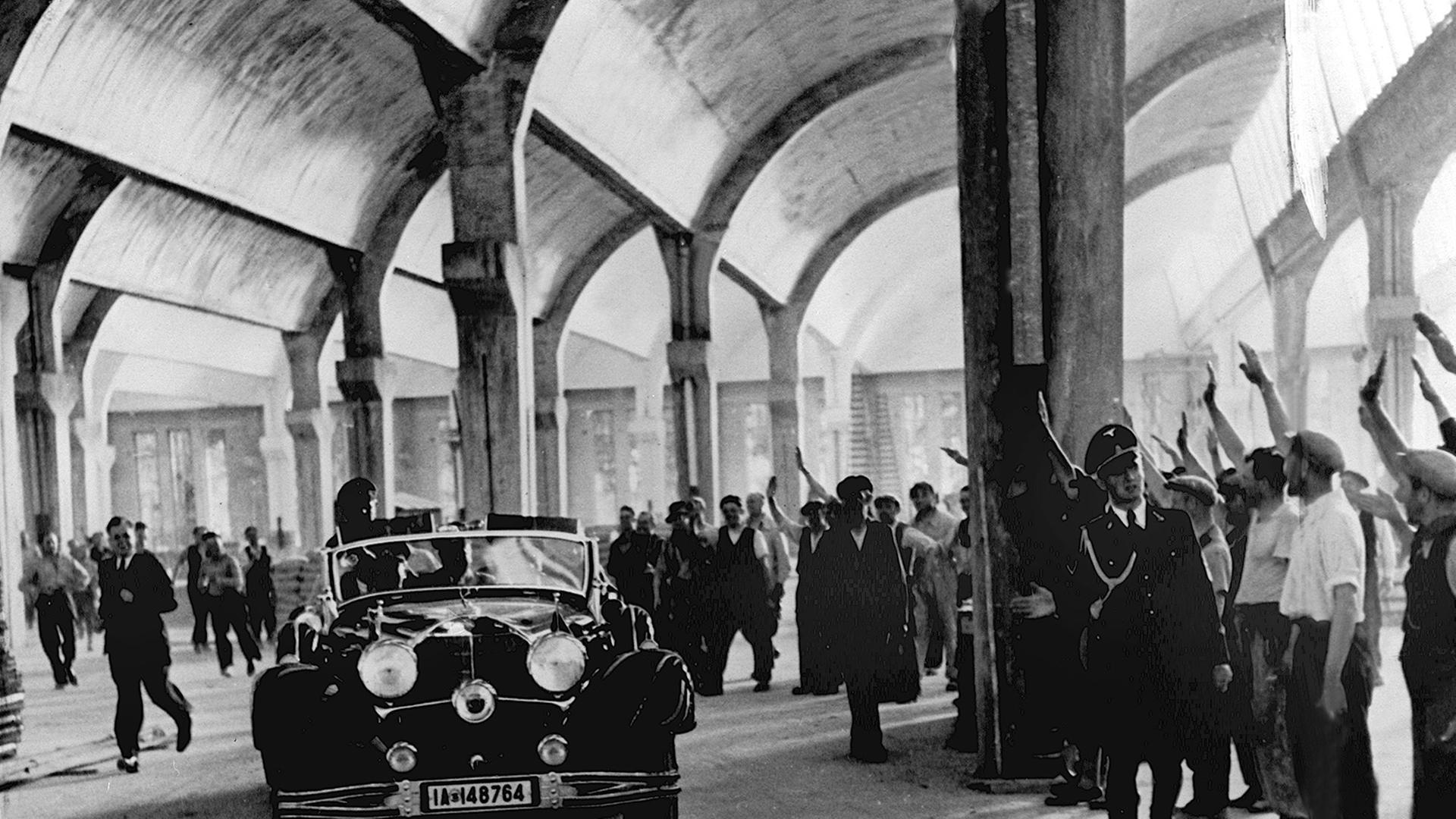 Reichskanzler Adolf Hitler wird bei seiner Fahrt im offenen Wagen durch das Wolfsburger Volkswagenwerk von den Arbeitern mit emporgereckten rechten Armen begrüßt. 