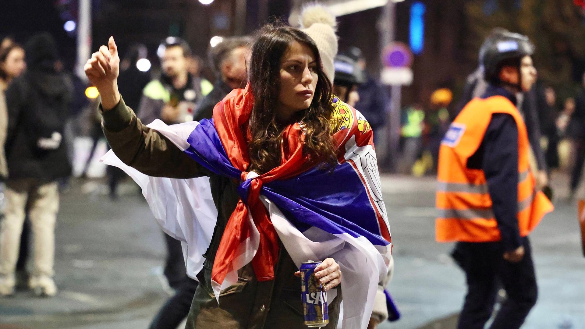 Eine junge Frau trägt eine serbische Flagge als Cape und hält die rechte Faust in die Luft