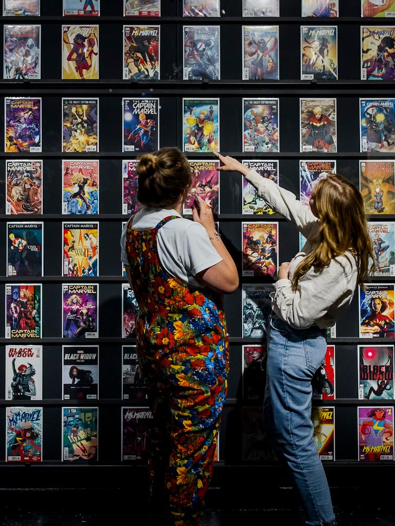 Zwei junge Frauen stehen vor einer Ausstellungswand mit den Covern von Superheldencomics.