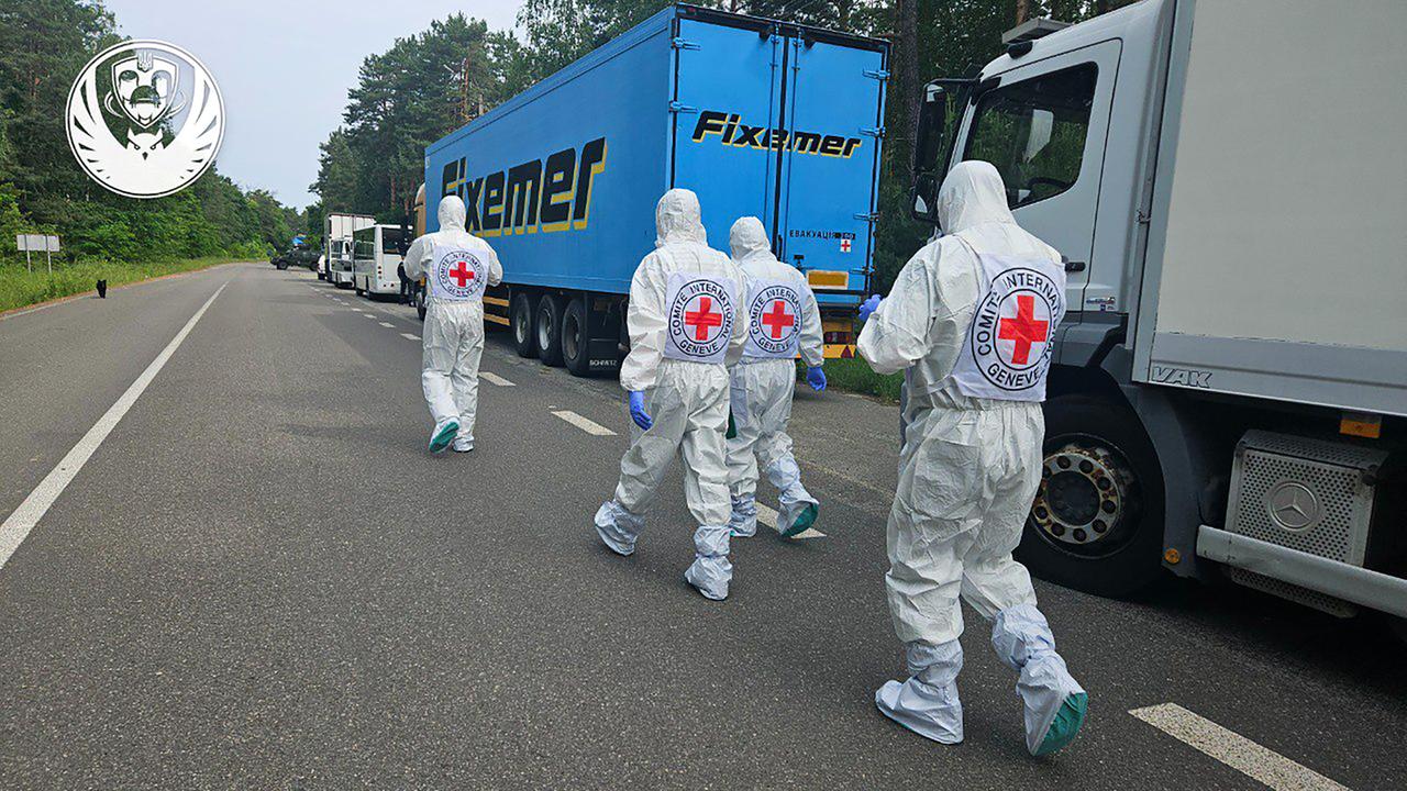 Menschen in Schutzkleidung gehen an Kühlwagen vorbei.