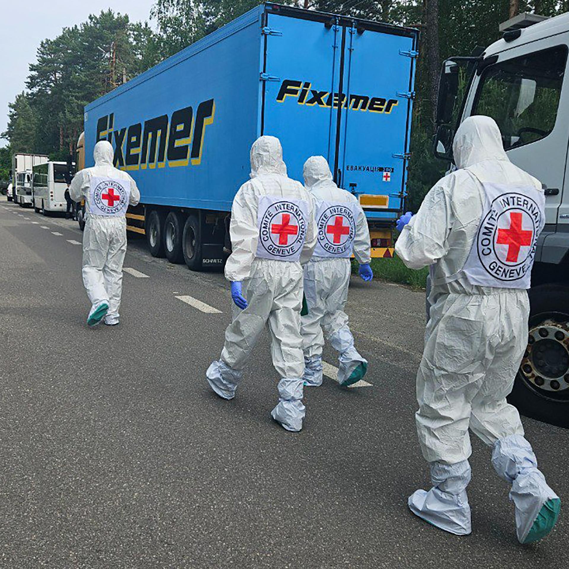 Mitarbeiter des Internationalen Komitees vom Roten Kreuz an einem unbekannten Ort, die an Kühlwagen vorbeigehen.