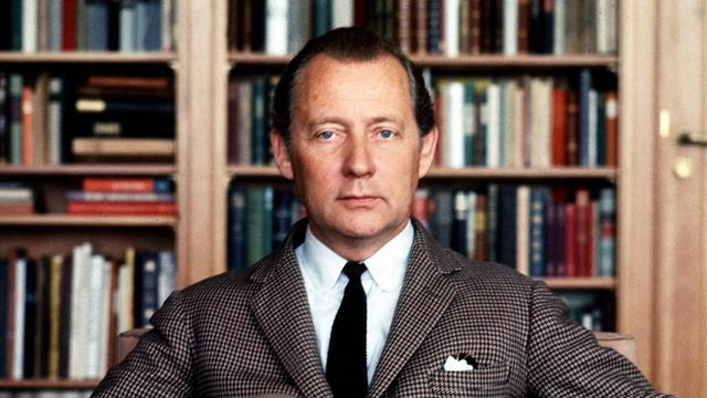 Axel Springer sitzt in herrschaftlicher Pose frontal vor der Kamera auf einem Sessel. Im Hintergrund ist eine Bücherwand.