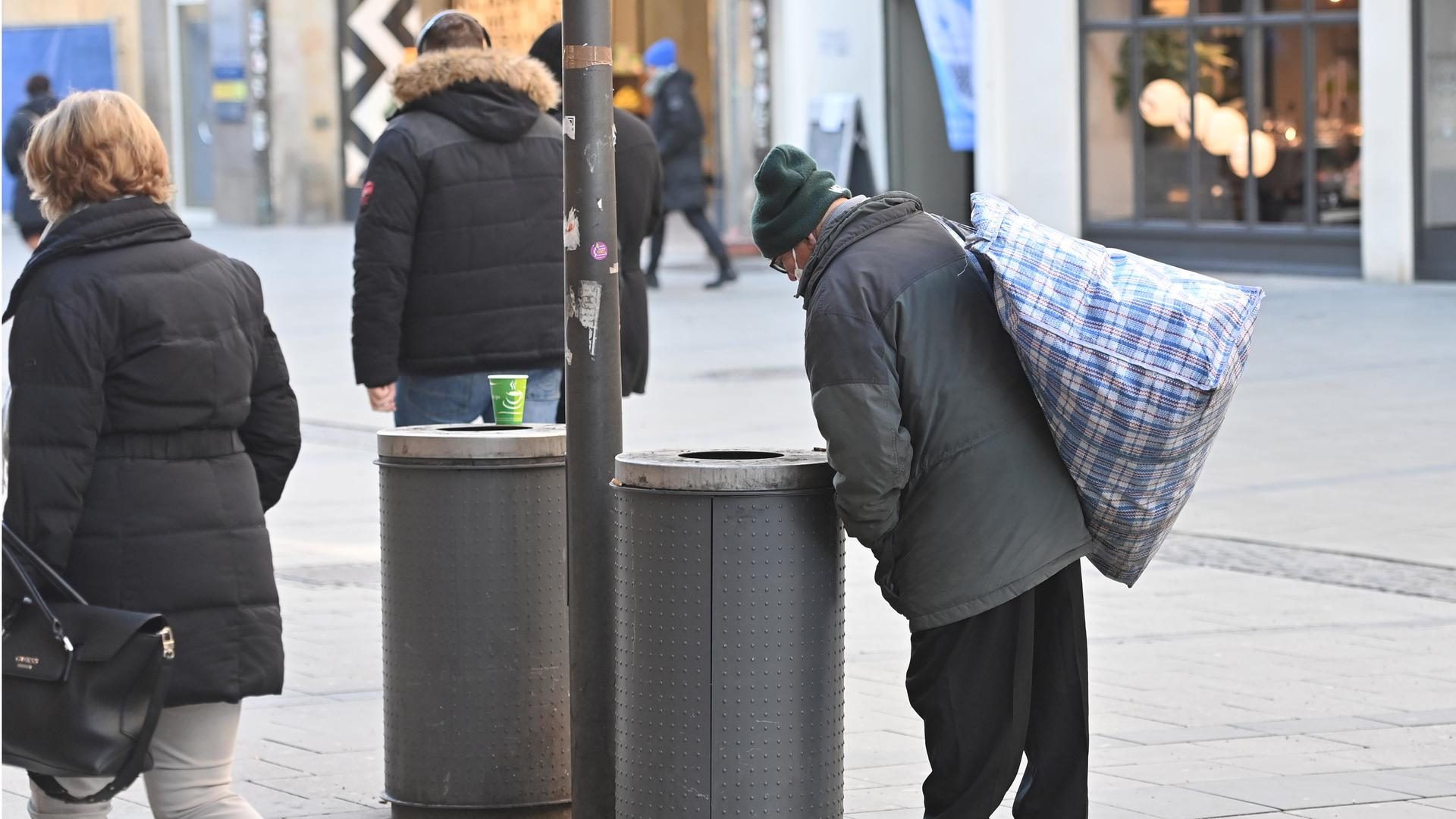 Ein alter Mann blickt in einen Abfalleimer in der Münchner Fussgängerzone und sucht nach Pfandflaschen. 