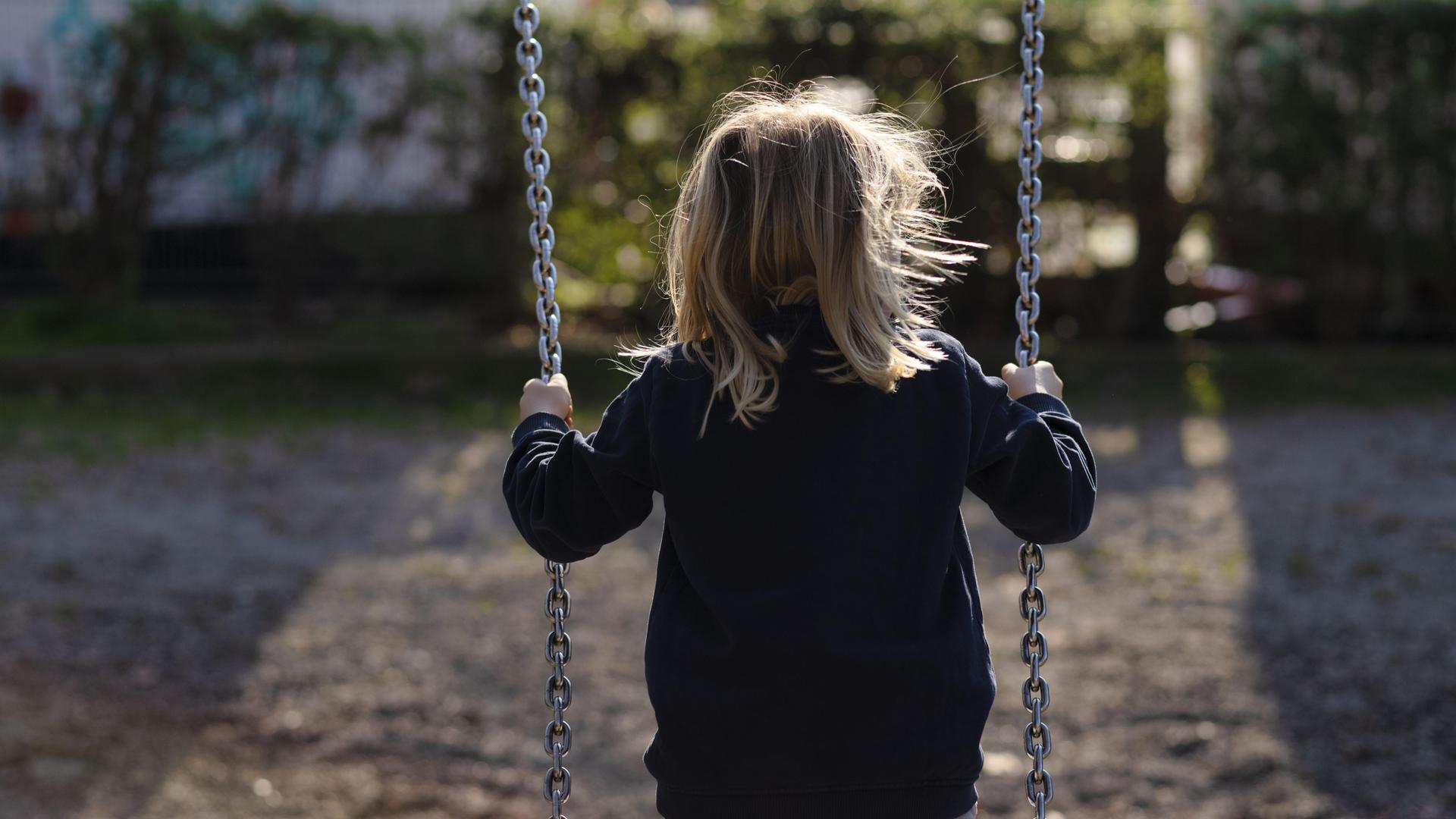 Ein blondes Mädchen schaukelt auf Schaukel. Man sieht es von hinten, der Hintergrund ist dunkel-verschattet. Ein blondes Mädchen schaukelt auf Schaukel. Man sieht es von hinten, der Hintergrund ist dunkel-verschattet.