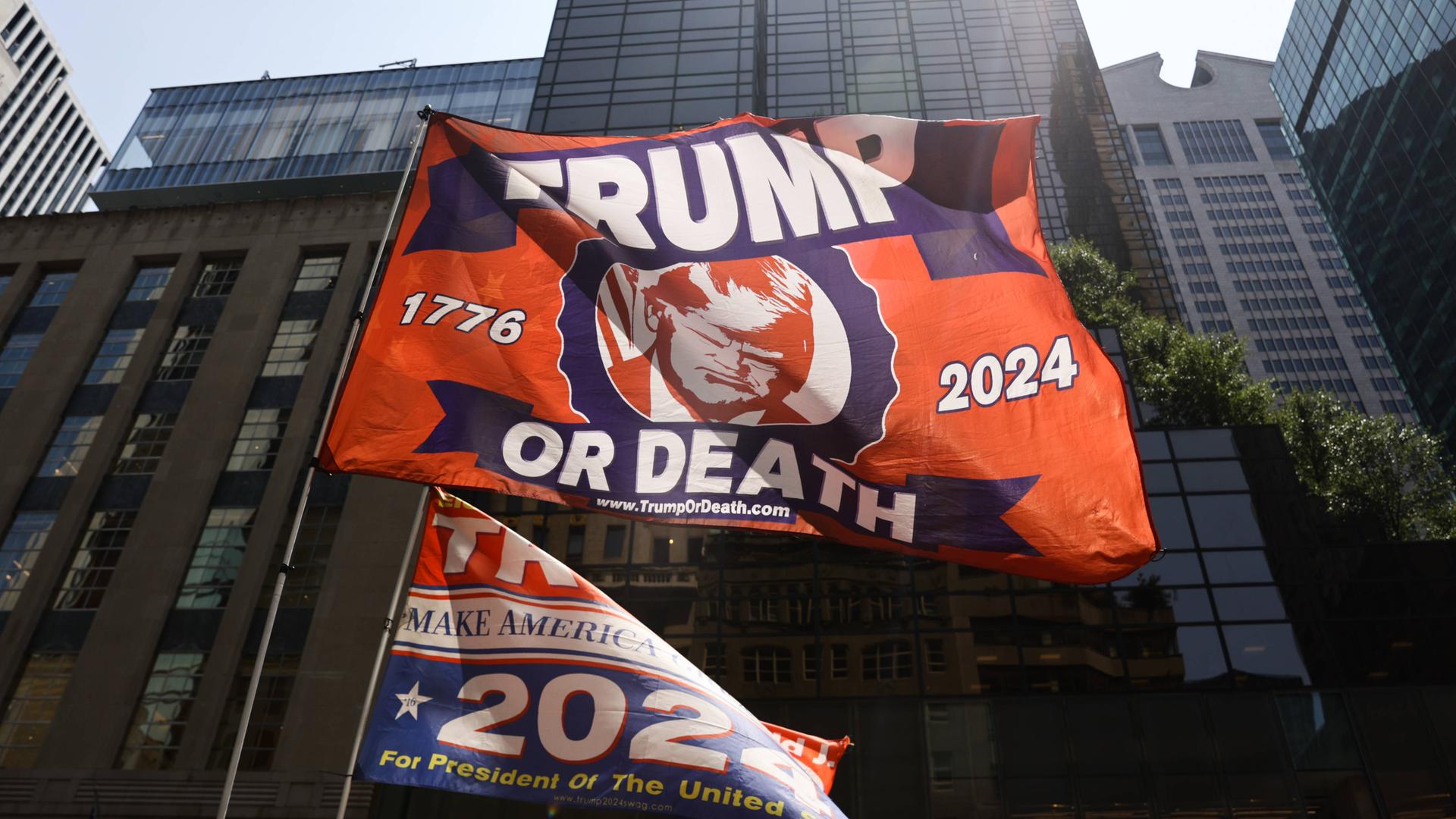 Vor dem Trump Tower hält ein Trump-Unterstützer am Tag nach dem Attentat auf Donald Trump eine Flagge auf der steht: Trump or Death, Trump oder Tod.