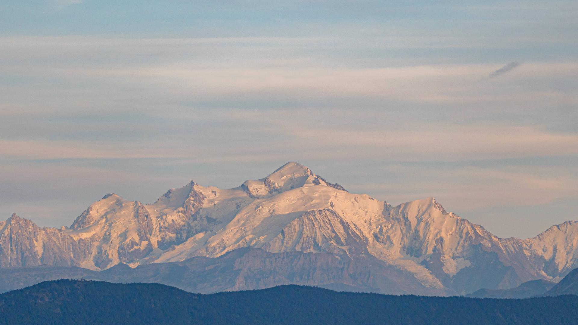 Panoramablick über den Mont Blanc, der durch das indirekte Licht des Sonnenuntergangs sanft rosa wirkt Panoramablick über den Mont Blanc, der durch das indirekte Licht des Sonnenuntergangs sanft rosa wirkt
