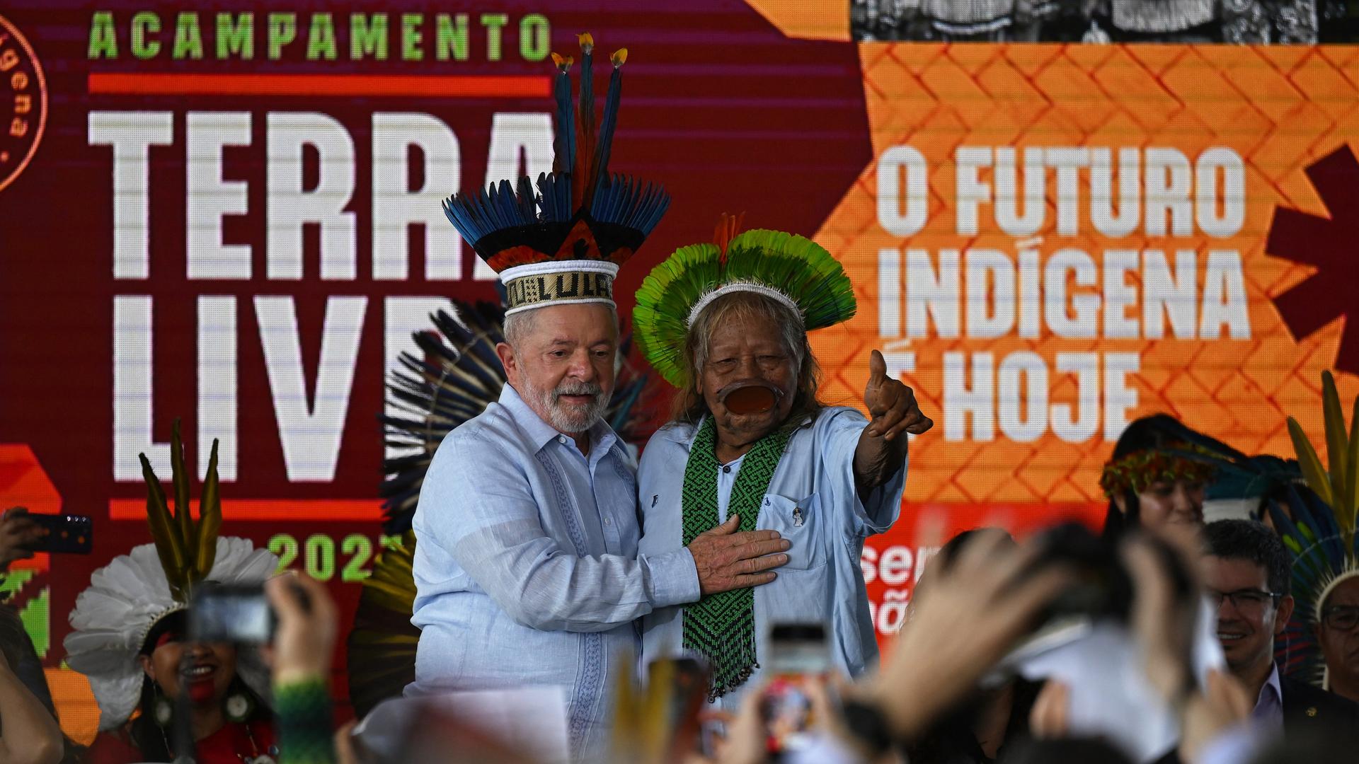 Das Bild zeigt den brasilianischen Präsidenten Lula da Silva zusammen mit Raoni Metuktire, dem Häuptling des Kayapo-Volkes. Beide tragen traditionellen Kopfschmuck aus Federn.