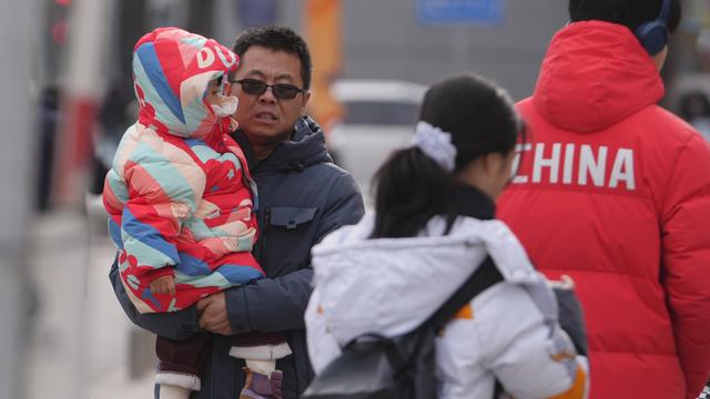 Ein Mann trägt ein Klein-Kind auf einer Straße in Peking. 