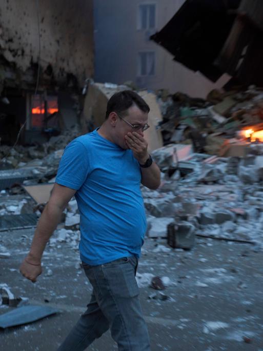 Ein Mann läuft in der ukrainischen Hauptstadt Kiew an einem brennenden Schutthaufen vorbei und hält sich die Hand vor das Gesicht. 