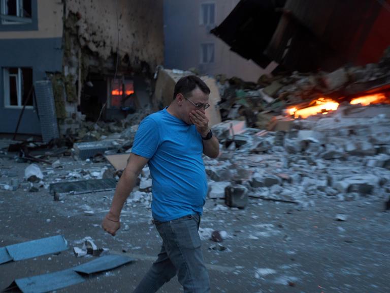 Ein Mann läuft in der ukrainischen Hauptstadt Kiew an einem brennenden Schutthaufen vorbei und hält sich die Hand vor das Gesicht. 