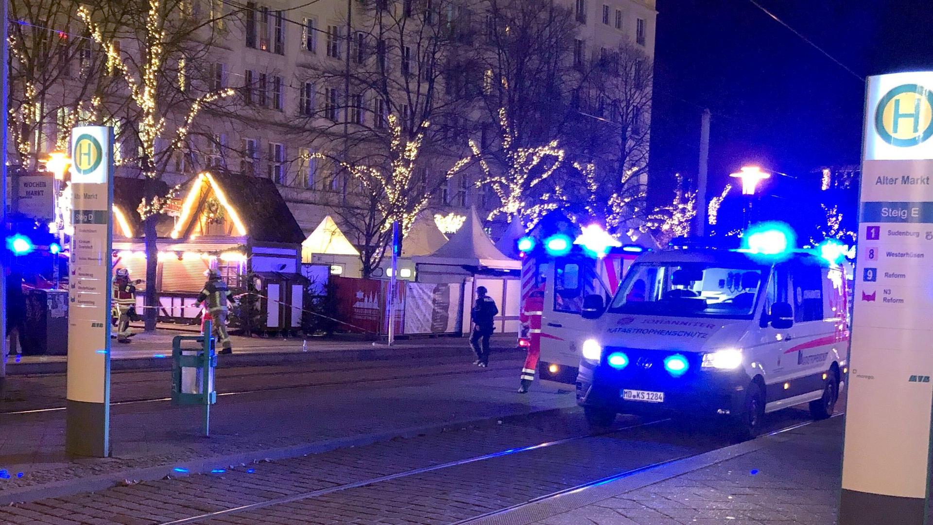 Einsatzkräfte von Rettungsdiensten sind in Magdeburg im Einsatz auf dem Weihnachtsmarkt. Vorne steht ein Rettungswagen, hinten sind Weihnachtsmarktbuden zu sehen. 