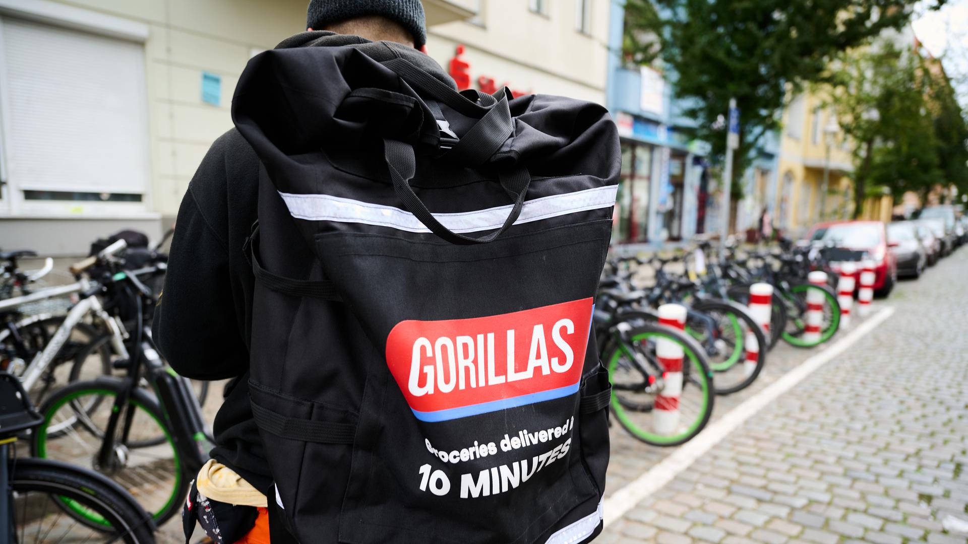Ein Beschäftigter des Lieferdienstes Gorillas trägt einen Rucksack und steht vor den Fahrrädern. 
