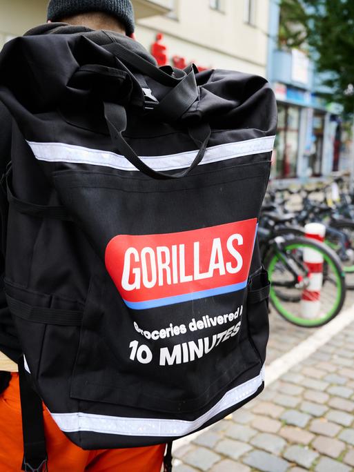 Ein Beschäftigter des Lieferdienstes Gorillas trägt einen Rucksack und steht vor den Fahrrädern. 
