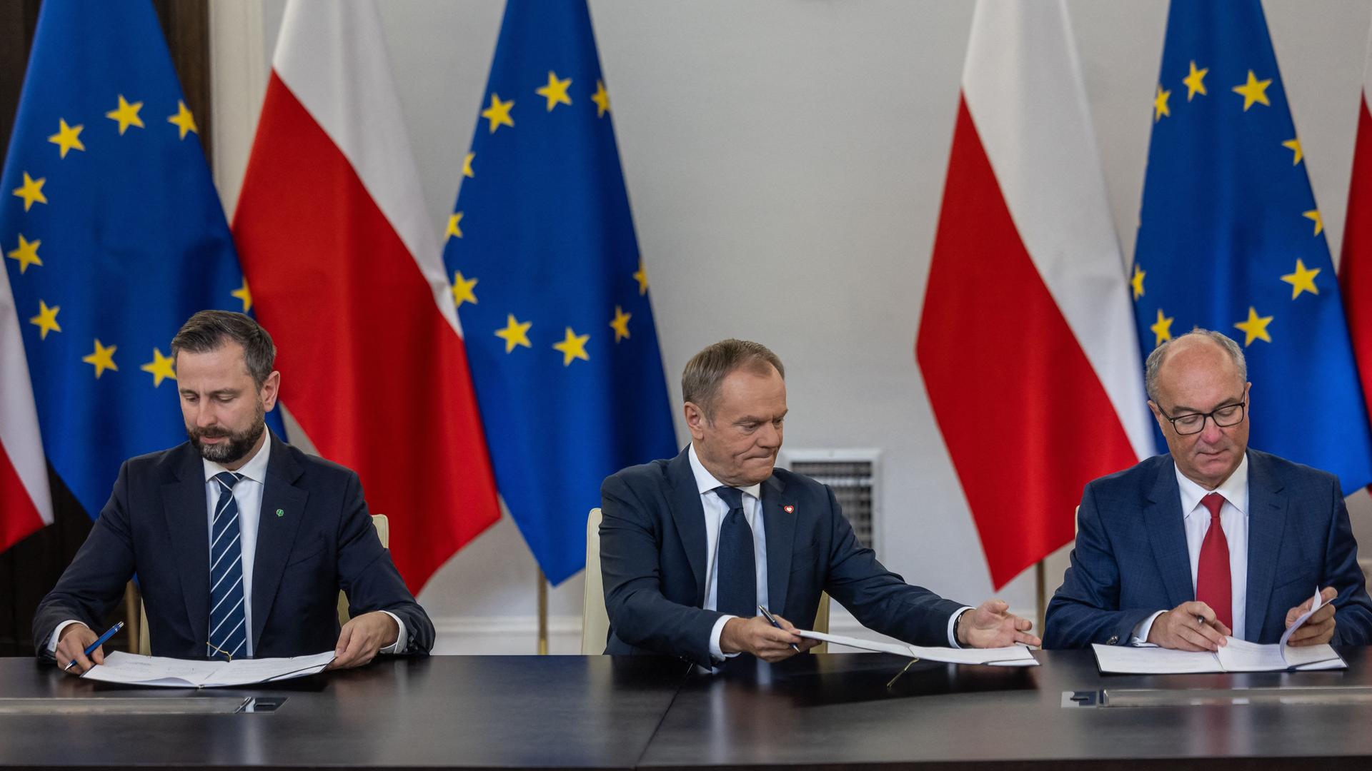 Die Führer der drei polnischen Oppositionsparteien unterzeichnen eine Koalitionsvereinbarung. Hinter ihnen polnische und EU-Flaggen.