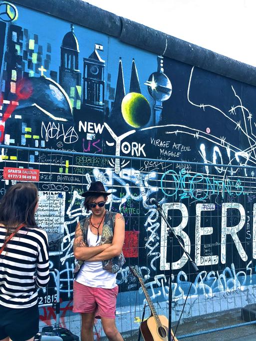 Blick auf die bemalte Mauer im Bereich der East Side Gallery mit Musiker und Publikum davor. Blick auf die bemalte Mauer im Bereich der East Side Gallery mit Musiker und Publikum davor.
