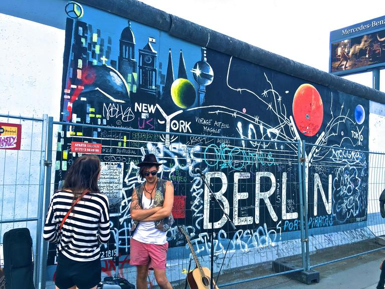 Blick auf die bemalte Mauer im Bereich der East Side Gallery mit Musiker und Publikum davor. Blick auf die bemalte Mauer im Bereich der East Side Gallery mit Musiker und Publikum davor.