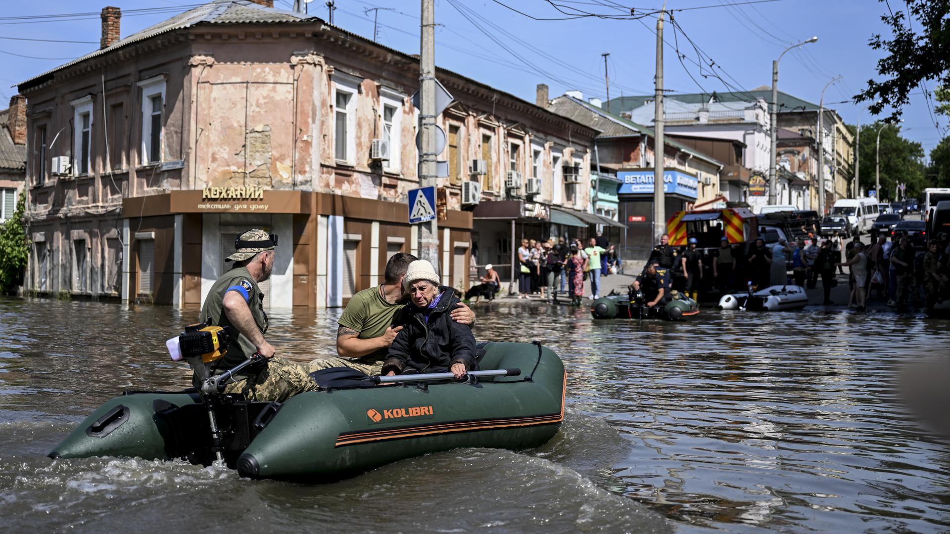 Helfer in einem motorisierten Schlauchboot fahren eine eine völlig überflutete Straße mit Wohnhäusern entlang.