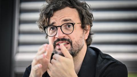 Julien Chavaz, Generalintendant des Theaters Magdeburg, während eines Interviews. Er trägt eine schwarze Brille, ein schwarzes Hemd, Bart und gestikuliert mit den Händen. Der Hintergrund ist verschwommen. Julien Chavaz, Generalintendant des Theaters Magdeburg, während eines Interviews. Er trägt eine schwarze Brille, ein schwarzes Hemd, Bart und gestikuliert mit den Händen. Der Hintergrund ist verschwommen.