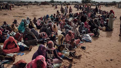 Viele Flüchtlinge aus dem Sudan sitzen im Tschad auf der Erde in einer langen Reihe.