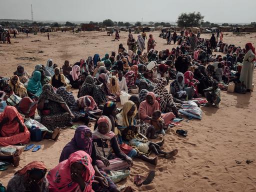 Viele Flüchtlinge aus dem Sudan sitzen im Tschad auf der Erde in einer langen Reihe.