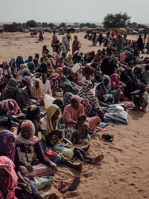 Viele Flüchtlinge aus dem Sudan sitzen im Tschad auf der Erde in einer langen Reihe.