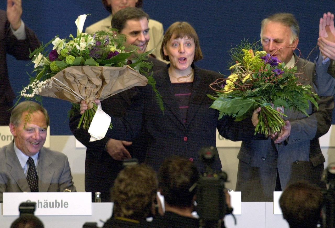 Angela Merkel jubelnd, mit zwei Blumensträußen in Händen.