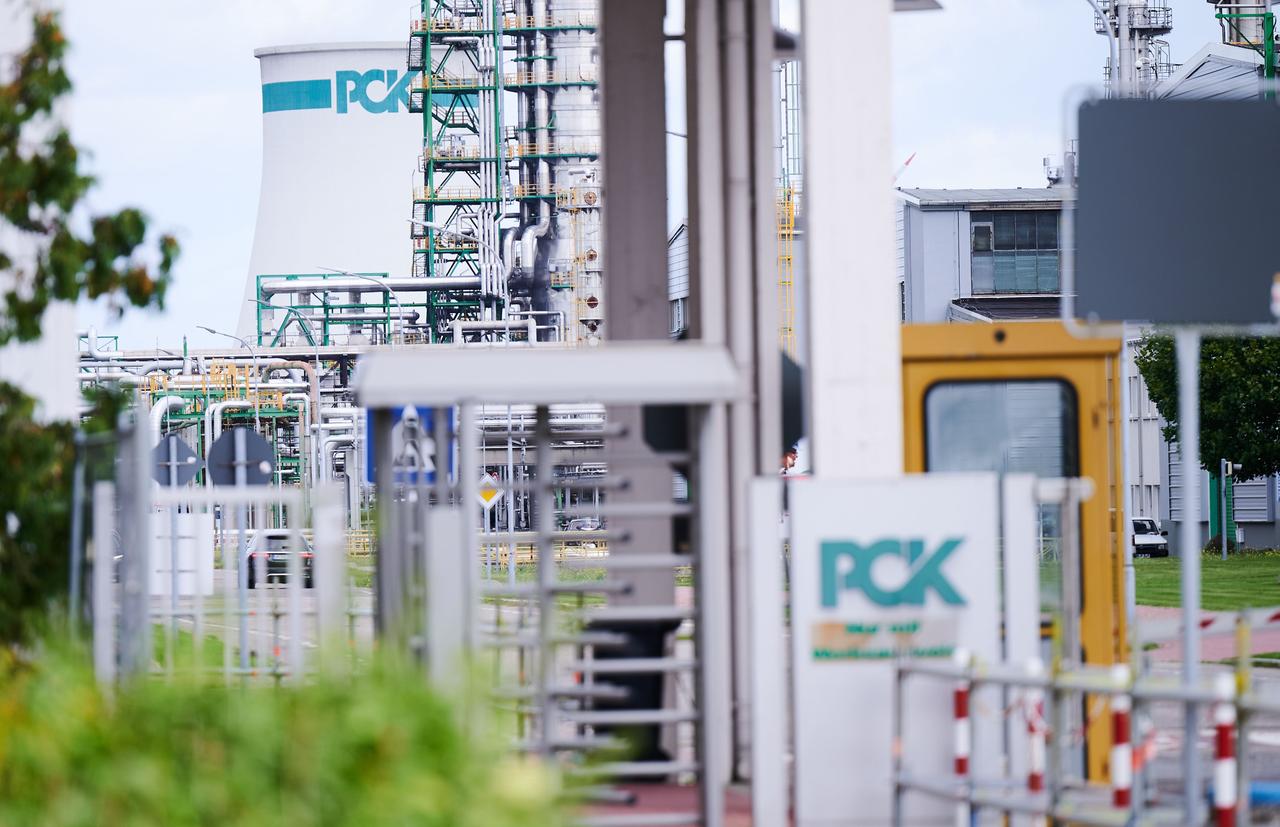 Das Bild zeigt das Werksgelände der Raffinerie PCK in Schwedt. Das Logo PCK ist im Vordergrund am Eingang zu sehen und im Hintergrund an einem Tank. 